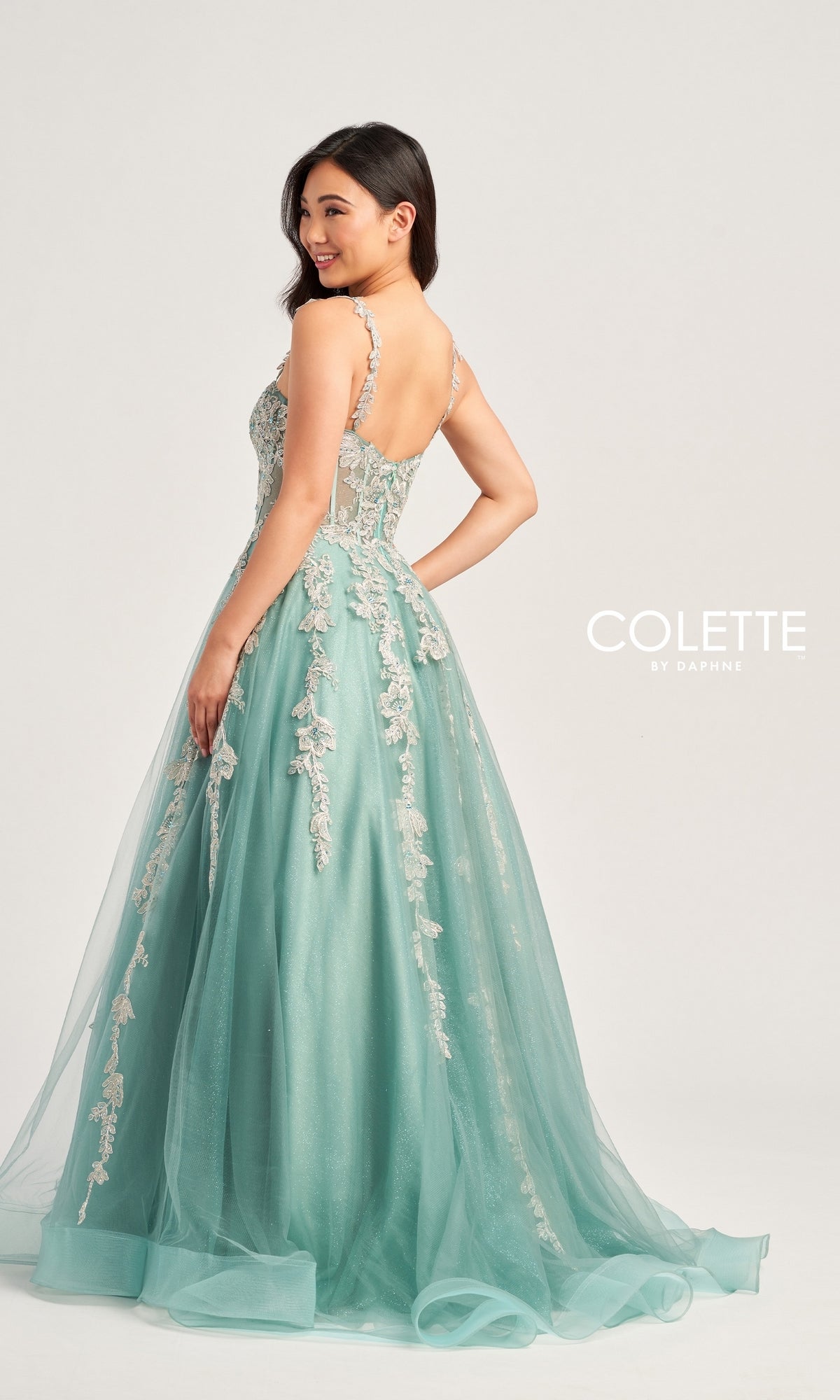 A woman in a light blue-green Metallic-Lace Colette Long Tulle Prom Dress (CL5165) with an embroidered tulle skirt poses, looking over her shoulder.